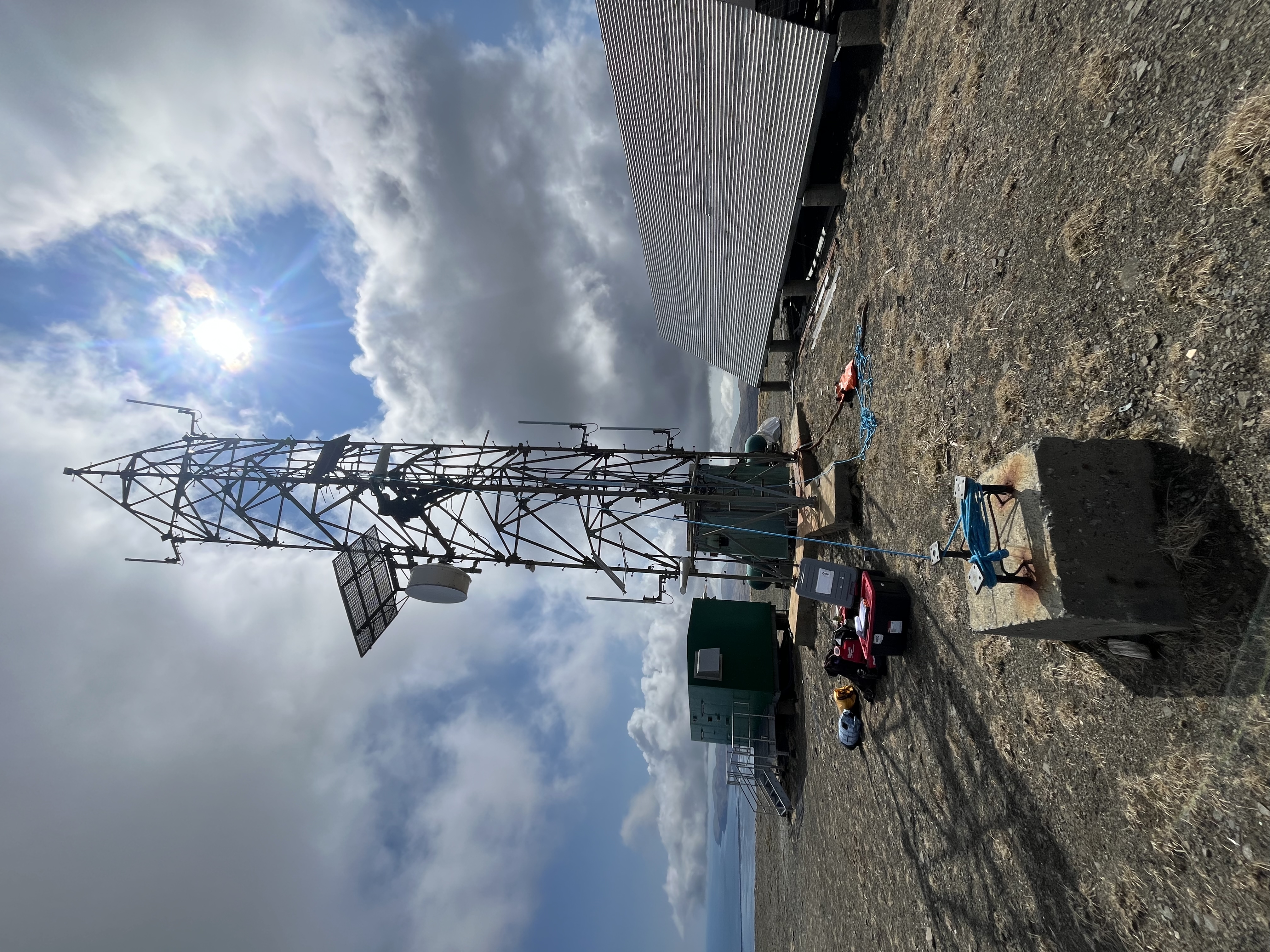 Metal communications tower on rocky ground.