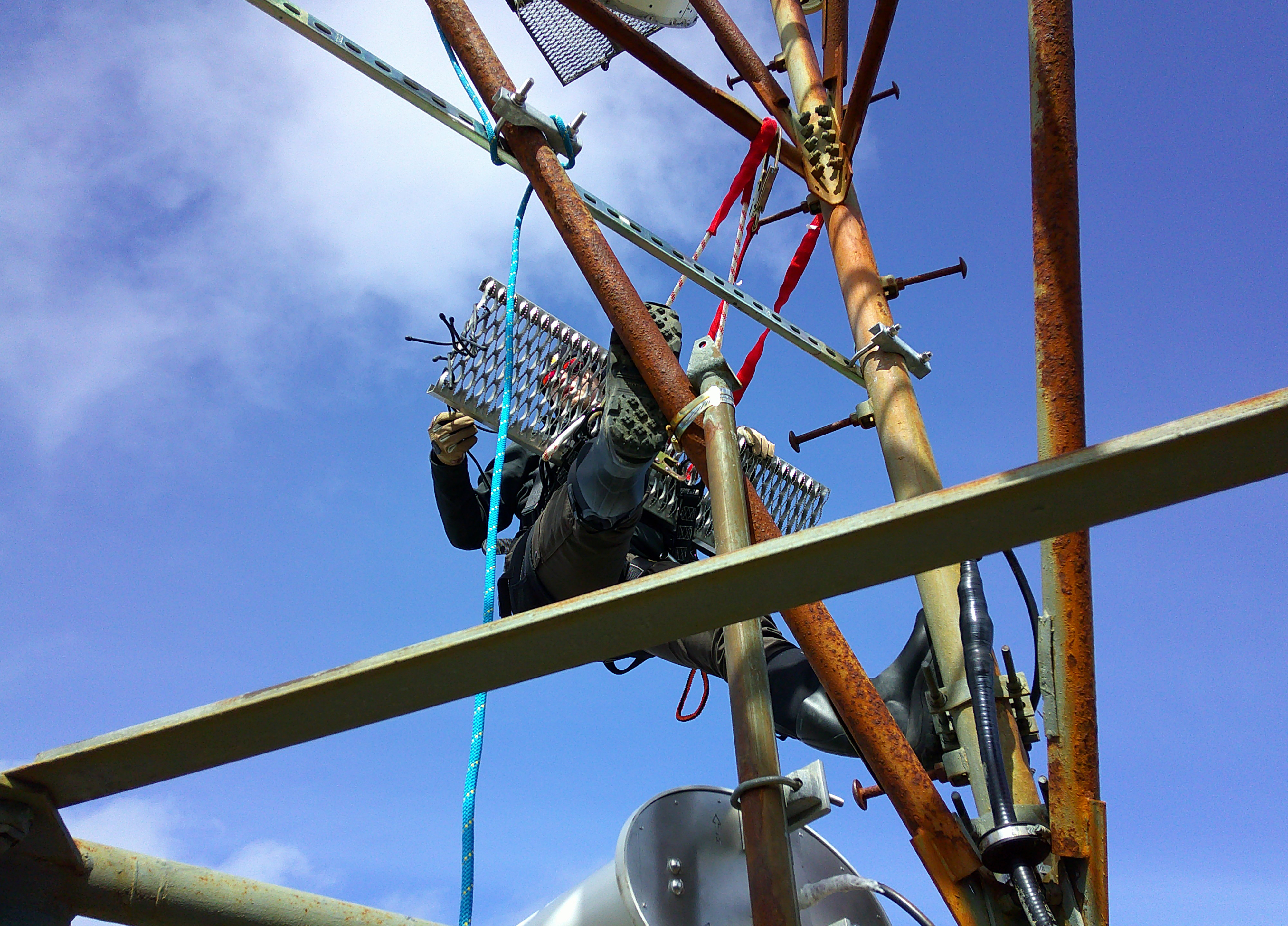 Person in climbing gear on metal tower holding metal grate.