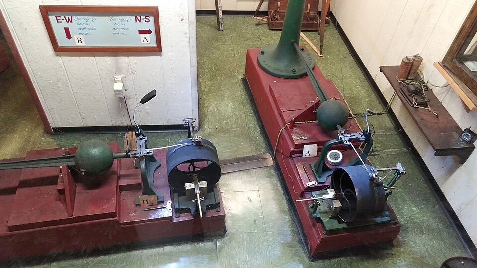 Two seismographs with large ball on horizontal arm attached to vertical post.