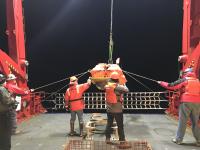 OBS Engineers and R/V Sikuliaq crew members are guiding sensor package into the water.