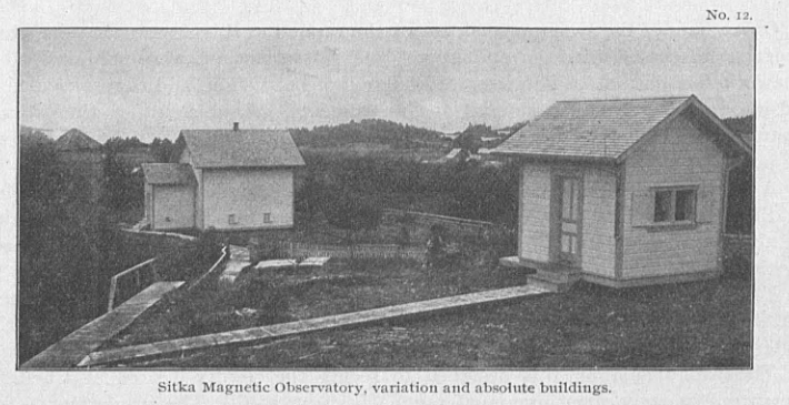 Old black-and-white photo showing two white buildings with wooden walkways between.