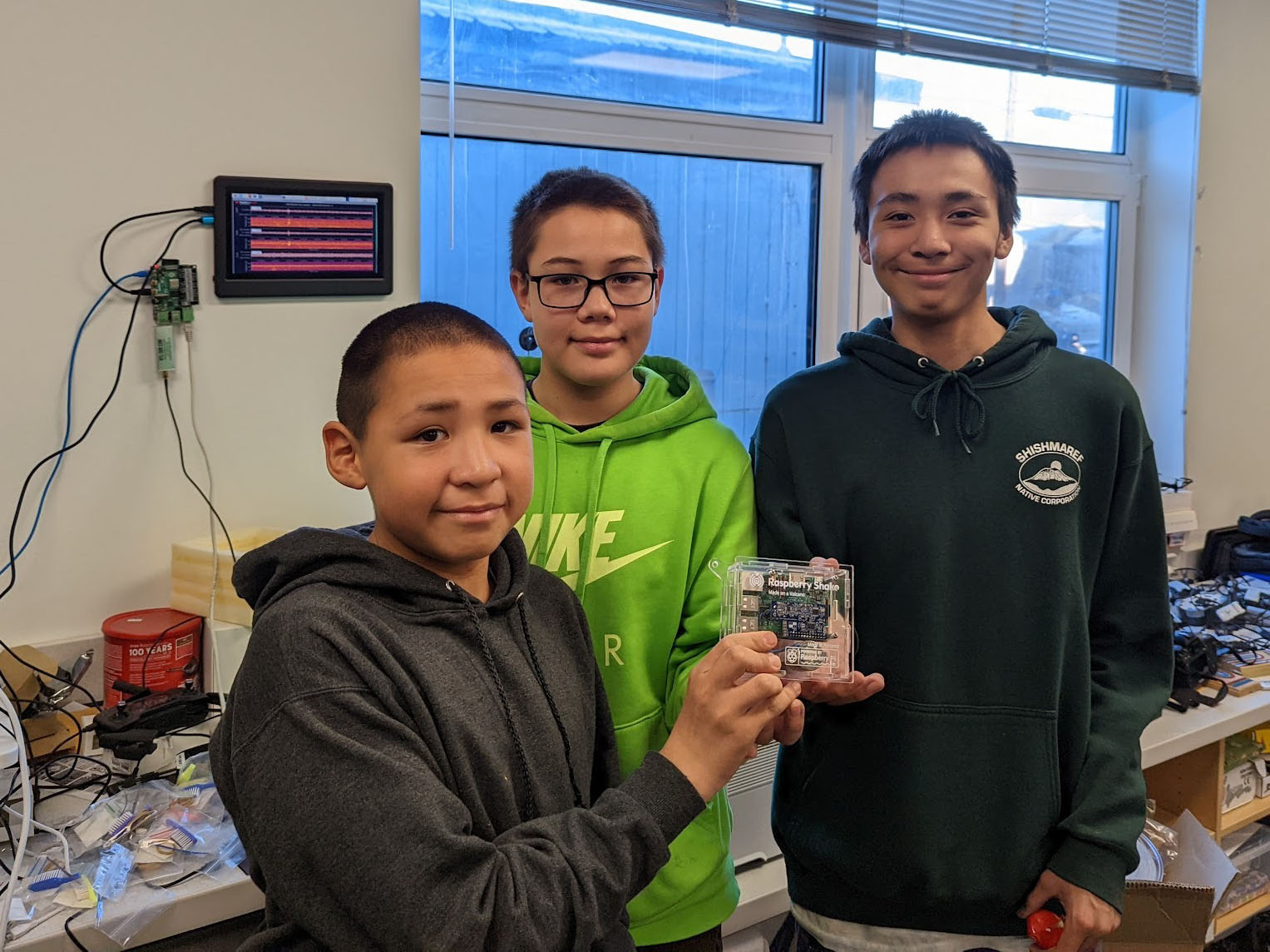 Three students holding up small Raspberry Shake seismometer